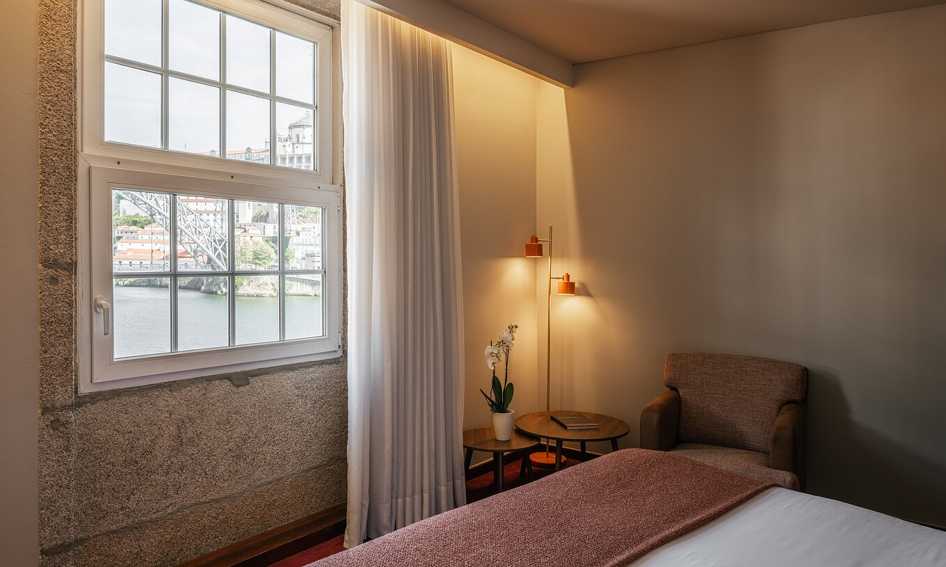 Quarto Plaza no Pestana Vintage Porto com janela ampla, vista para o rio, poltrona e iluminação suave